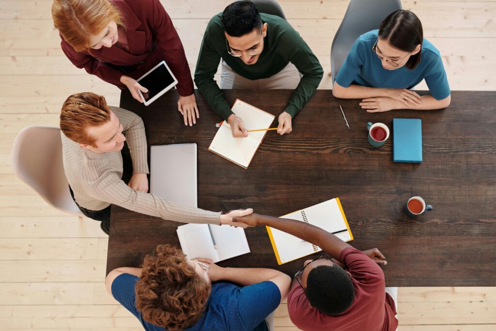 pexels photo 6147028 6147028 1 Top view of a diverse business team meeting with a handshake across the table. Collaborative working environment.